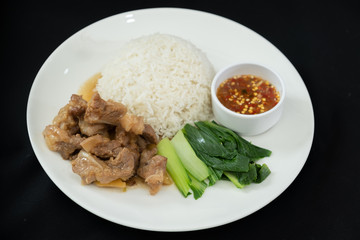 Stewed pork with rice, spicy sauce and vegetables. Black background 