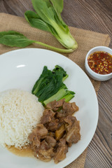 Stewed pork with rice, spicy sauce and vegetables. Wooden table