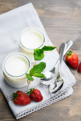 Two glasses of natural yogurt on a wooden table are decorated with mint and strawberries.