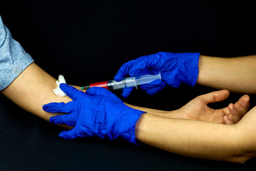 The doctor takes a blood test from a patient on a black background. The test for the coronavirus.