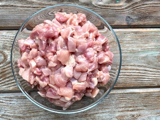 Chicken meat cut into small pieces in a transparent plate, on a wooden background.