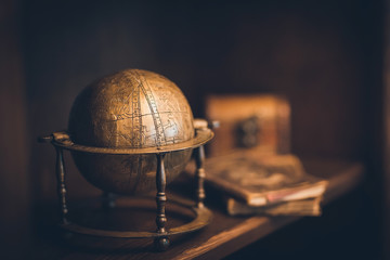 Fototapeta na wymiar vintage globe made of copper, in the background a chest and books