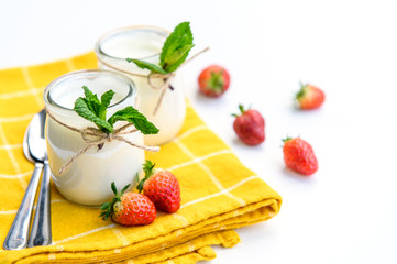 Two glasses of natural yogurt on a white background decorated with mint and strawberries.