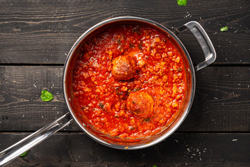 Meatball tomato sauce in stainless pan. Meatball tomato sauce cooked in a stainless steel saucepan placed on a dark black wooden background. This homemade meat based pasta sauce is a nice red color.