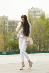Obraz premium Fashion style portrait of young beautiful elegant brunette woman walking at city streets on a windy dull day.
