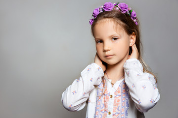 Portrait of posing pretty little girl in white dress and purple wreath on gray isolated background . 