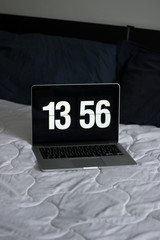 open laptop computer with vintage clock on a white bed and blue pillows vertical
