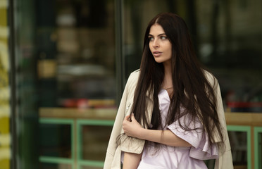 Fototapeta premium Fashion style portrait of young beautiful elegant brunette woman walking at city streets on a windy dull day.