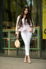 Fashion style portrait of young beautiful elegant brunette woman walking at city streets on a windy...