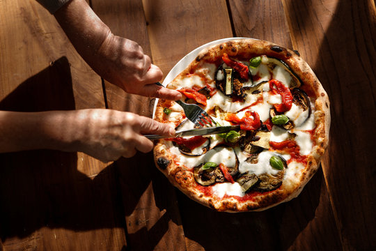 Mani tagliano una fetta di pizza al gusto "ortolana"  isolata sopra un tavolo in legno