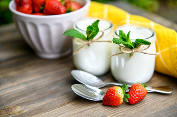 Two glasses of natural yogurt with chia on a wooden table are decorated with mint and strawberries.