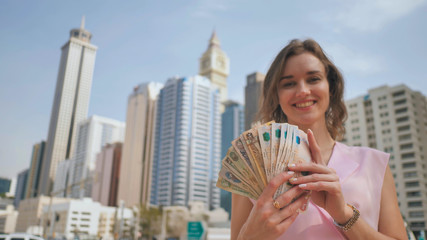 The girl holds in her hands the money of the United Arab Emirates on the background of the city...