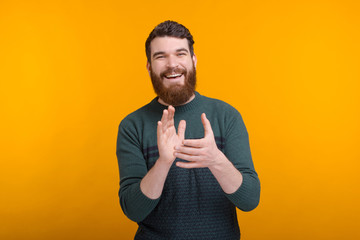 Cheerful smiling bearded man is applausing on yellow background.