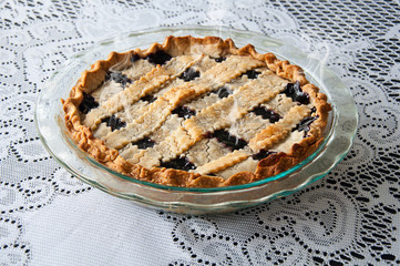 Fresh hot blueberry pie in a glass pie pan on a lace tablecloth.  Steam coming off this lattice crust homemade dessert.