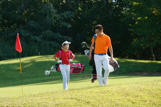 The coach on the pitch and students walk carrying a golf bag