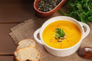 Pumpkin soup and parsley on rustic wooden table. Seasonal autumn food - Spicy pumpkin ans carrot soup.