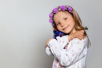 Portrait of happy little girl in white dress and purple wreath with plush unicorn toy on gray isolated background. Look at camera 
