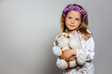 Portrait of pretty little girl  in white dress and purple wreath with plush tiger toy on gray isolated background. Look at camera 