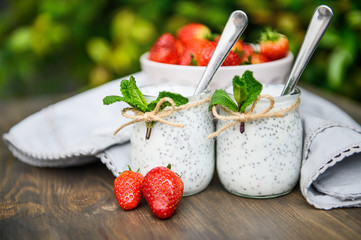 Two glasses of natural yogurt with chia seeds on a wooden table are decorated with mint and strawberries. Good morning note. Selective focus.
