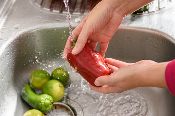 Lavando um pimentão vermelho, vista lateral de uma pessoa higienizando um legume com água na pia,...