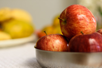 Maças dentro de uma vasilha de metal e no fundo, frutas desfocadas.