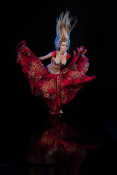 Young woman belly dancer in a red oriental costume on a black background