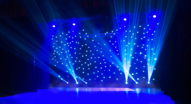 Blurred show background. Empty stage and sparkling stage lights. Blue light beams spotlights on stage at time of entertainment show. Laser and lights show in the dark