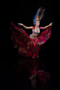 Young woman belly dancer in a red oriental costume on a black background