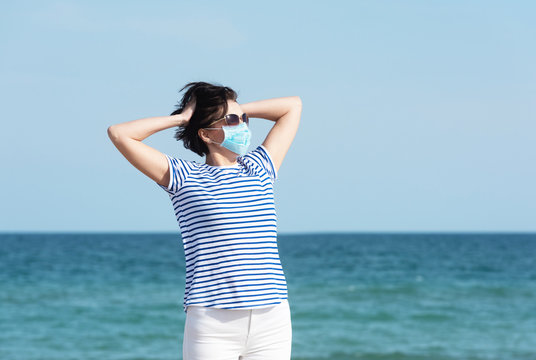 Young woman in a mask standing on empty coast, protective equipment during coronavirus covid19. Social distance concept.