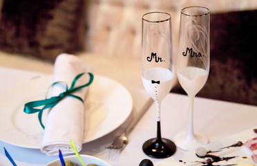 Two glasses of champagne are on the wedding table. The glasses are next to each other and they say Mr and Mrs