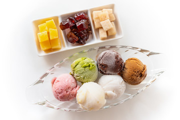 Top view multi-colored ice cream in a clear dish and sweet processed fruit for eating together in vintage Thai style, Set of colorful ice cream scoops of different colors on the white table background