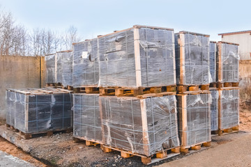 A pile of building materials packaged in cellophane film and pallets in an industrial area
