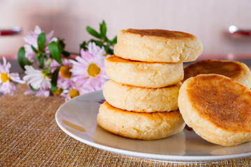 Cottage cheese pancakes with sour cream and jam on a brown background. Breakfast dish next to flowers.