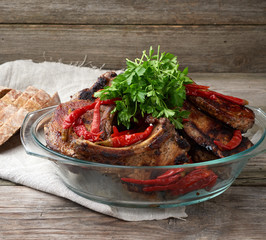 grilled pork steaks on the bone lie in a transparent glass plate on a wooden table