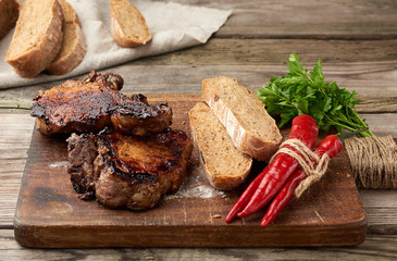 grilled pork steaks on the bone on a kitchen cutting board, baked sliced rye flour bread