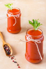 two tomato smoothies in glass jars with wooden spoon with pepper on a wooden background