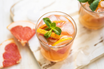 Grapefruit cocktails with mint and ice. Cold summer citrus fresh beverage on light wooden background