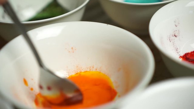 Spoon stir orange paint powder in white bowls plates. Easter eggs painting