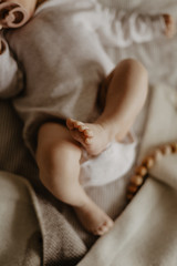 legs of a baby lying on a beige plaid and wooden toys on the background