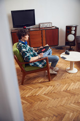 Handsome guy with vinyl record sitting in armchair at home