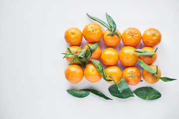 Orange fresh tangerines or mandarines with green leaves lie on a white background. Top view. Copy space.