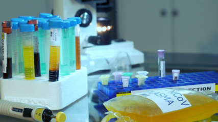 An IV bag of blood plasma and other serum samples for possible treatment of COVID19 lying on a laboratory table.