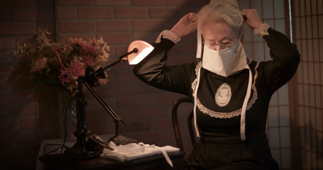 An old woman sitting in her home tries out the face mask she has handmade to wear during the 1918...