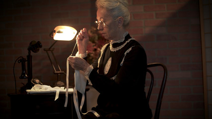 An old woman sitting in her home making a homemade face covering or mask to wear because of the...
