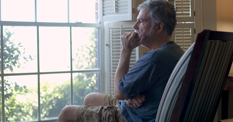 An older man stares out the window during coronavirus pandemic depressed about business closures and financial woes.