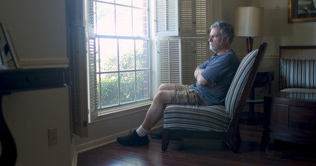 Depression setting in for this mature man sitting by his window feeling isolated and fearful during the coronavirus pandemic business closures as well as market woes.