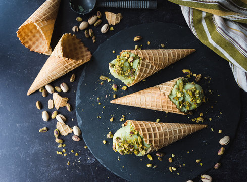 Overhead view of pistachio ice cream in cones on black background.