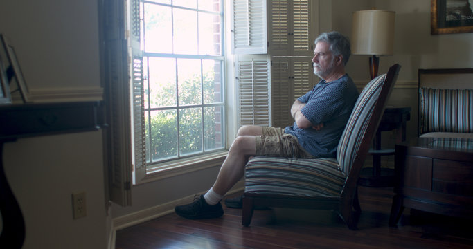 Depression setting in for this mature man sitting by his window feeling isolated and fearful during the coronavirus pandemic business closures as well as market woes.