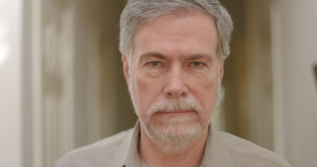 A mature white bearded man with a grim expression on his face staring straight into the camera walks slowly in to focus.