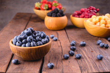 Blueberries and other berries in bowls on a dark wooden background.